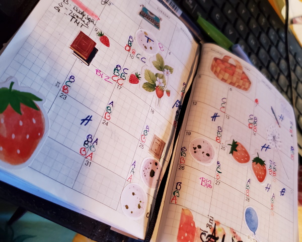 A two-page monthly spread in planner decorated with different strawberry stickers. Each day shows three letters in different colours