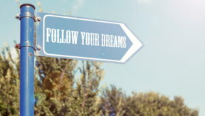 A blue street sign says Follow Your Dreams