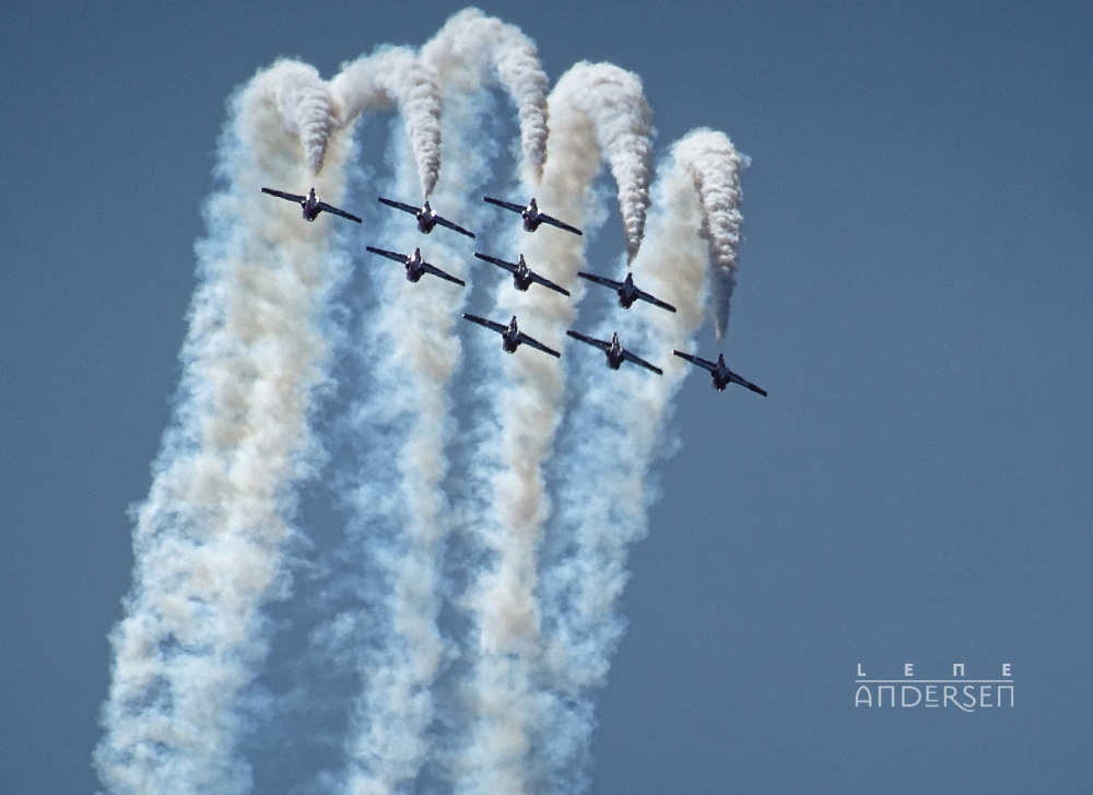 Snowbirds in formation flying straight up, then over and down. Contrails show the path gainst a blue sky