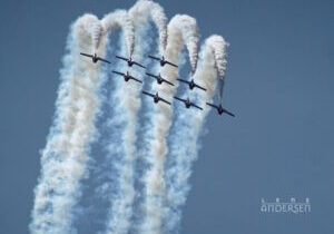 Snowbirds in formation flying straight up, then over and down. Contrails show the path gainst a blue sky